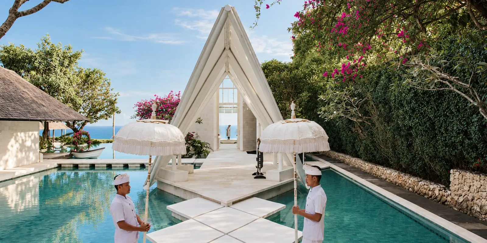 A glass wedding chapel above the ocean in Bali, reached across a turquoise pool